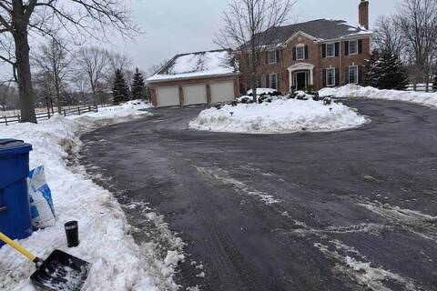 A cleared circular driveway in front of a two-story brick house with an attached three-car garage, snow banked on the center island